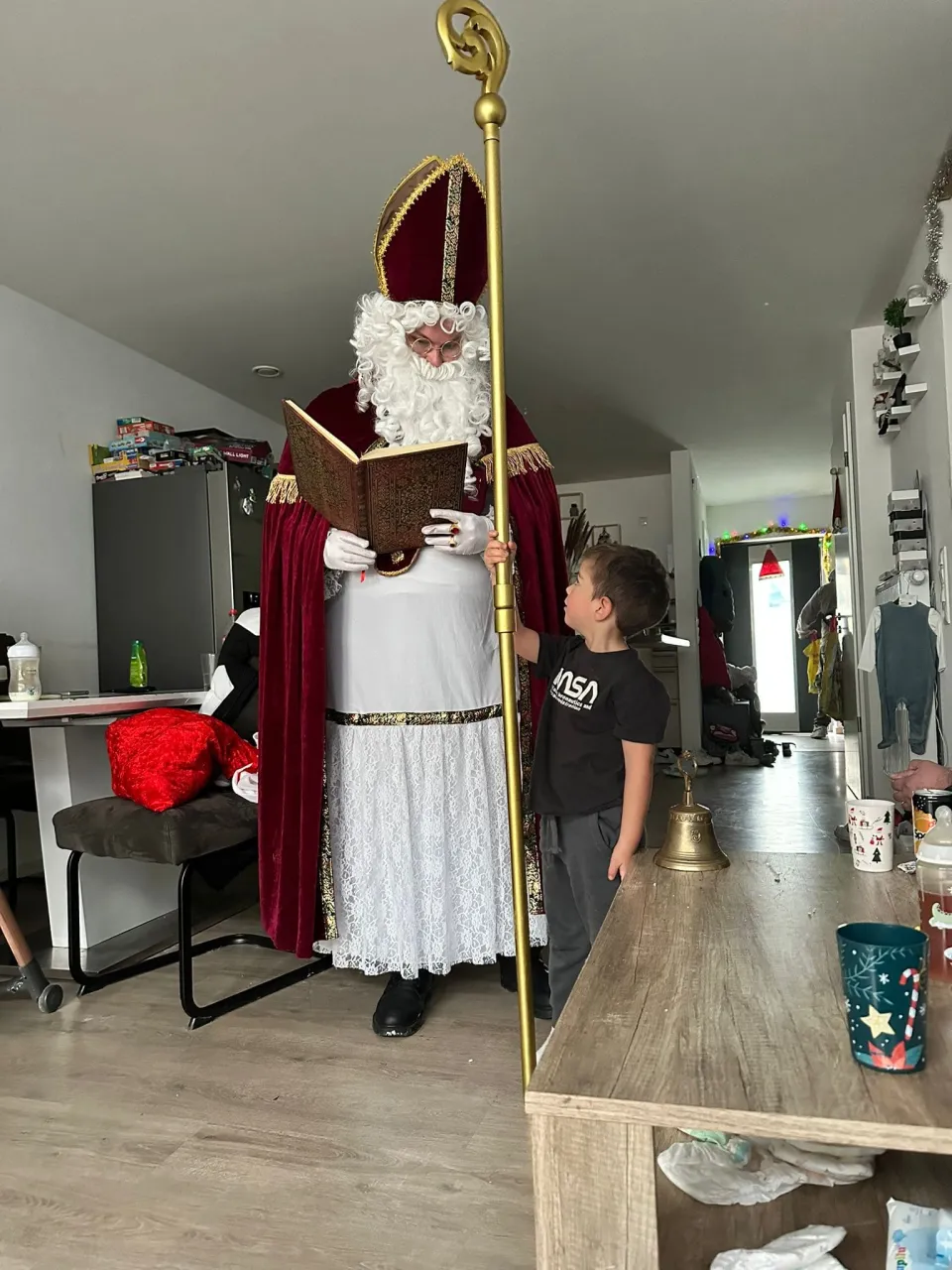Nikolaus liest aus dem goldenen Buch vor während der Junge nebendran steht und den Bischofsstab festhält.