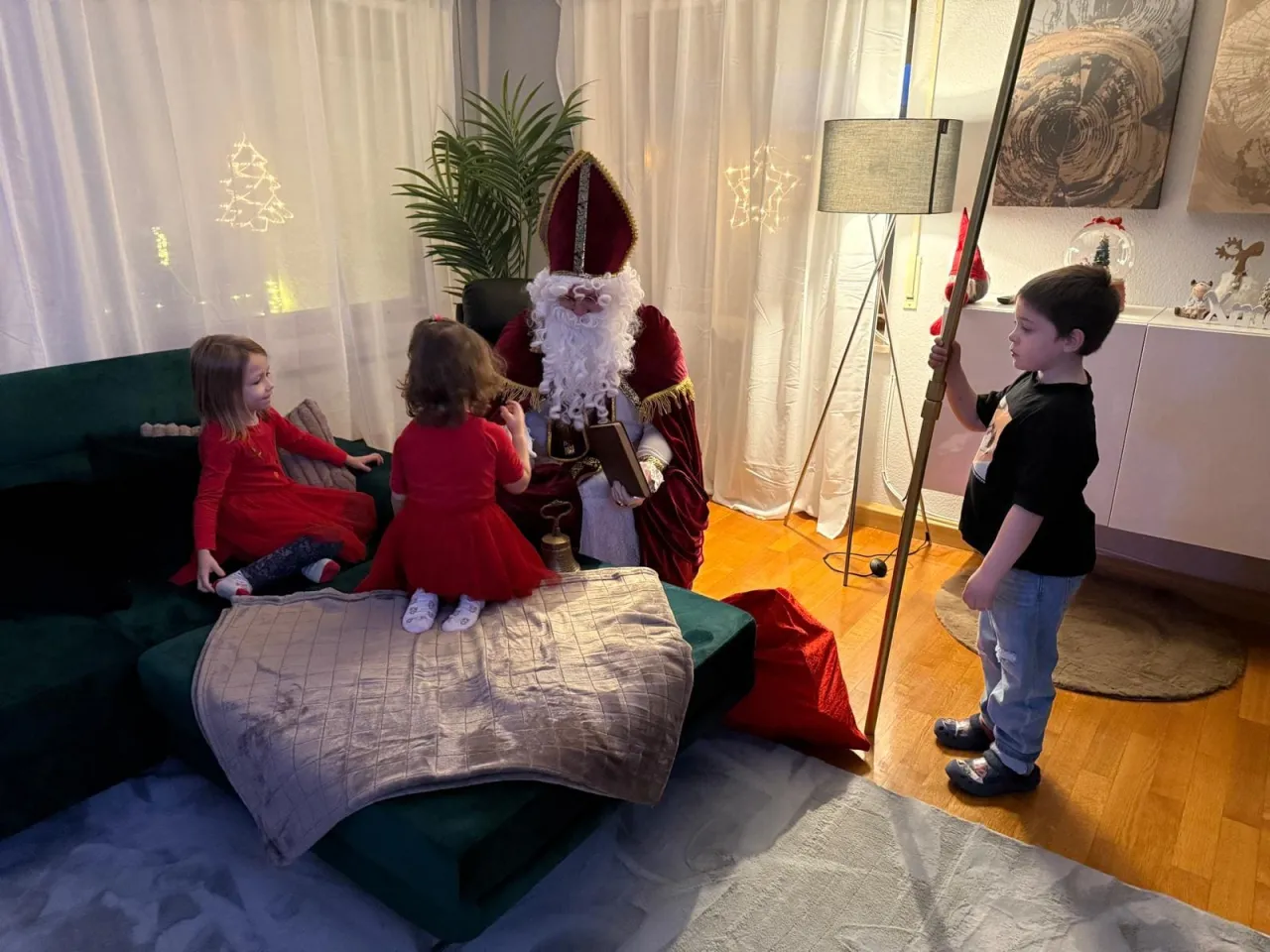 Ein Junge hält den Bischofsstab während sich zwei kleine Mädels mit dem Nikolaus reden.