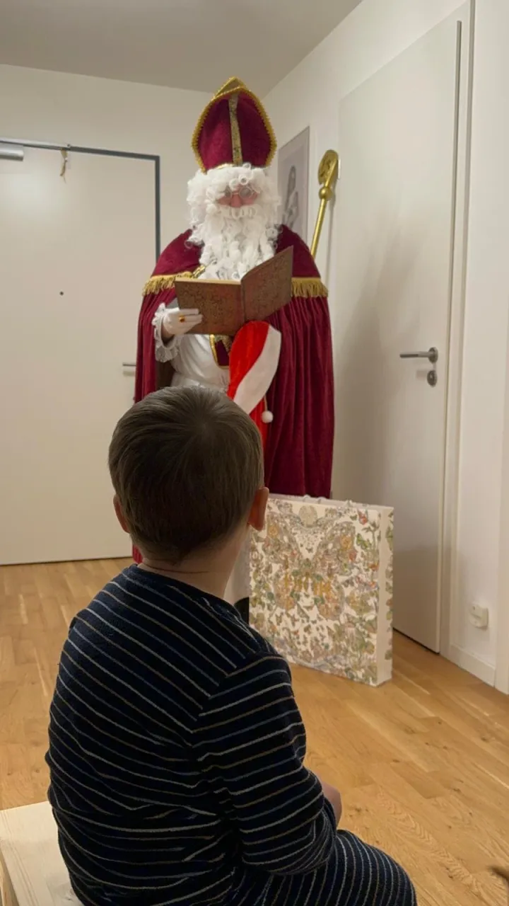Ein Junge sitzt vor dem Nikolaus während dieser aus dem goldenen Buch vorträgt.