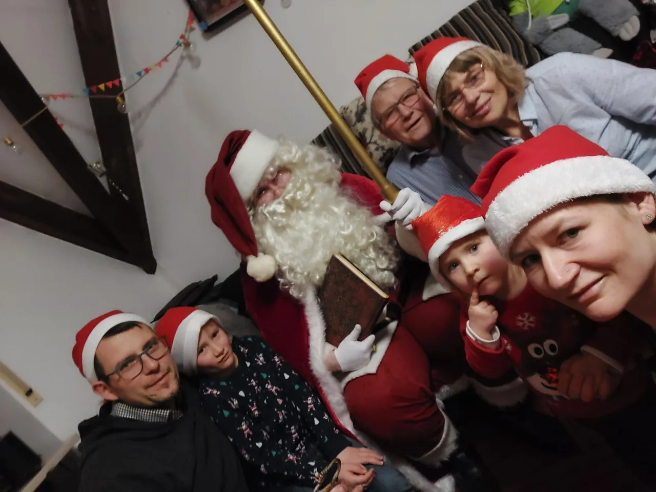 Familie trägt Weihnachtsmützen während sie ein Foto mit Weihnachtsmann machen.