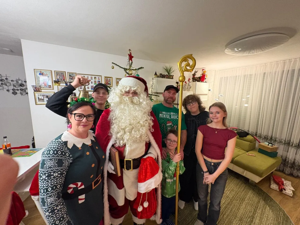 Gruppenfoto vom Weihnachtsmann mit einer Familie mit 6 Personen, der Kleinste hält den Stab vom Weihnachtsmann.