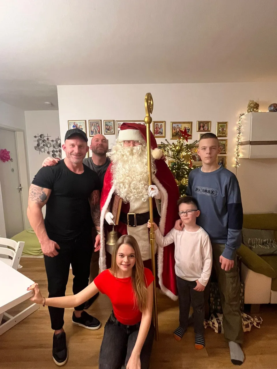 Gruppenfoto vom Weihnachtsmann mit einer Familie mit zwei Erwachsenen und drei Kindern, der Kleinste hält den Stab vom Weihnachtsmann.