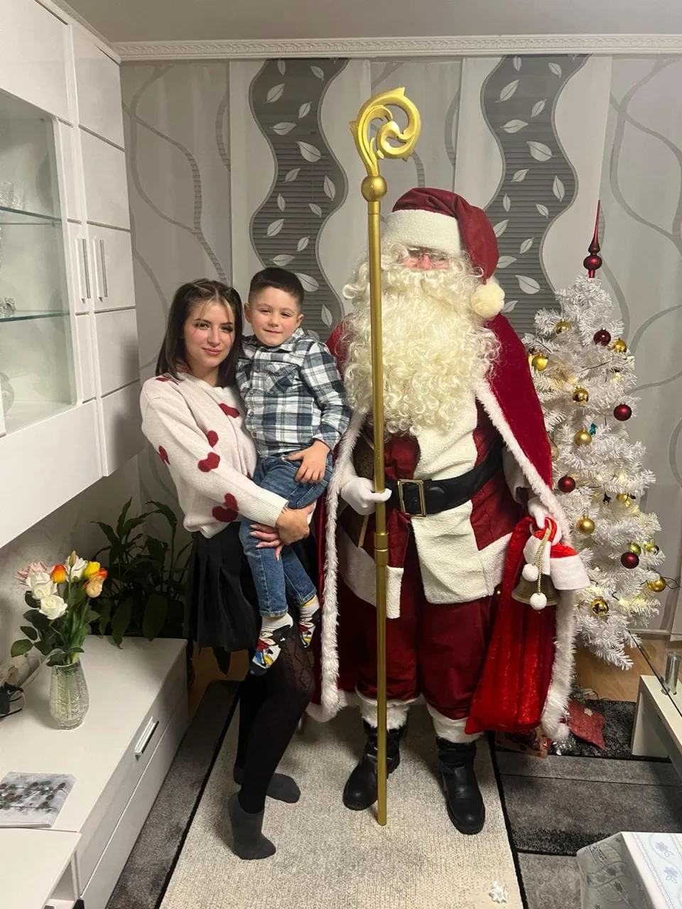 Weihnachtsmann neben einem Weihnachtsbaum zusammen mit Mutter und Kind.