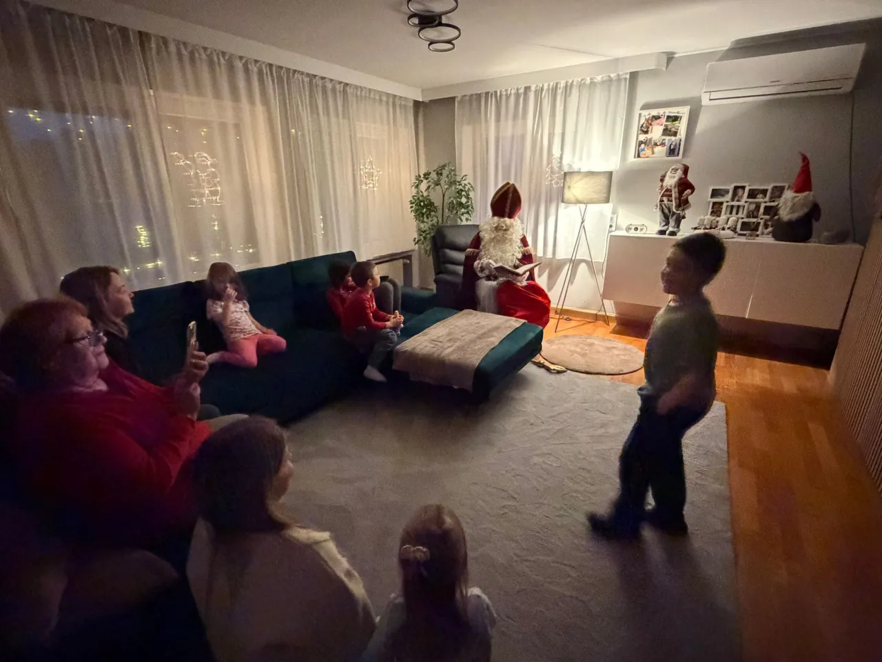 Familie aus Erwachsenen und Kindern sitzen auf der Couch während der Nikolaus aus seinen goldenen Buch vorträgt.