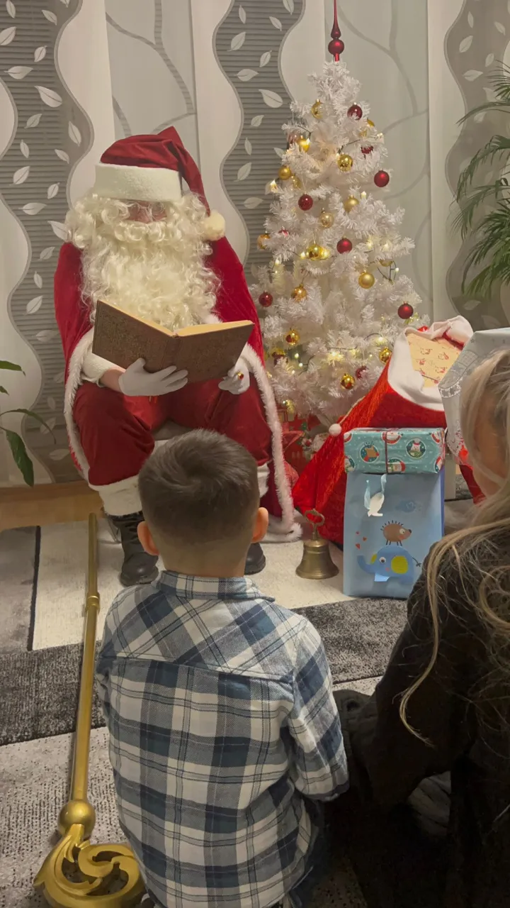 Weihnachtsmann trägt aus dem goldenen Buch vor während ein Junge zuhört.