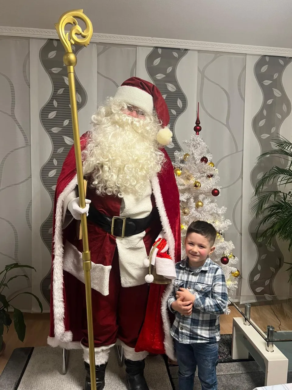 Weihnachtsmann zusammen mit einem Jungen vor einem Weihnachtsbaum.